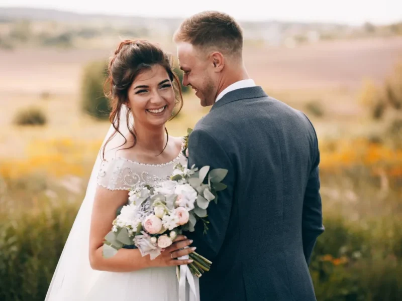 A bride and groom in a field with a bouquet of flowers.