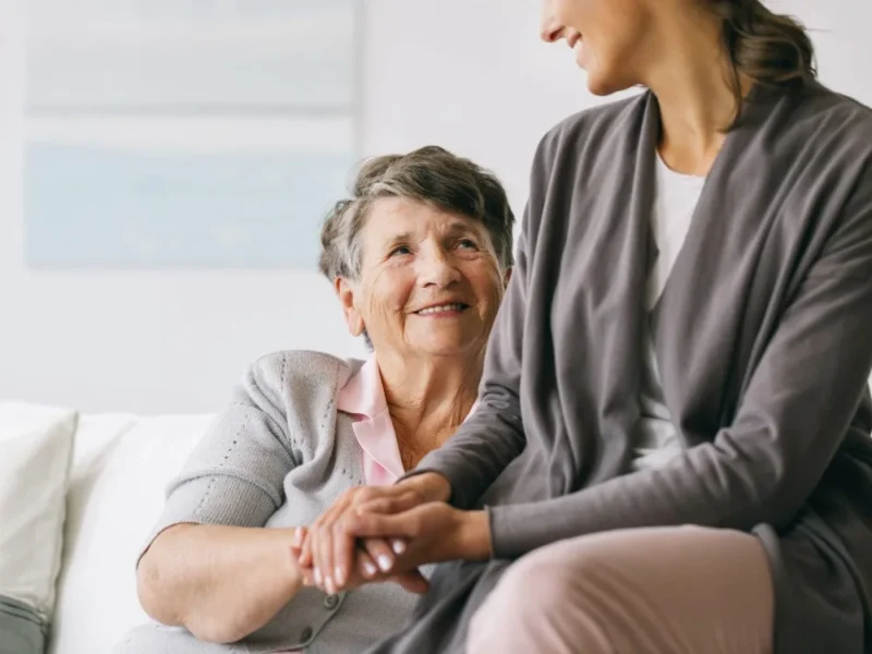 An older woman holding the hand of her carer.