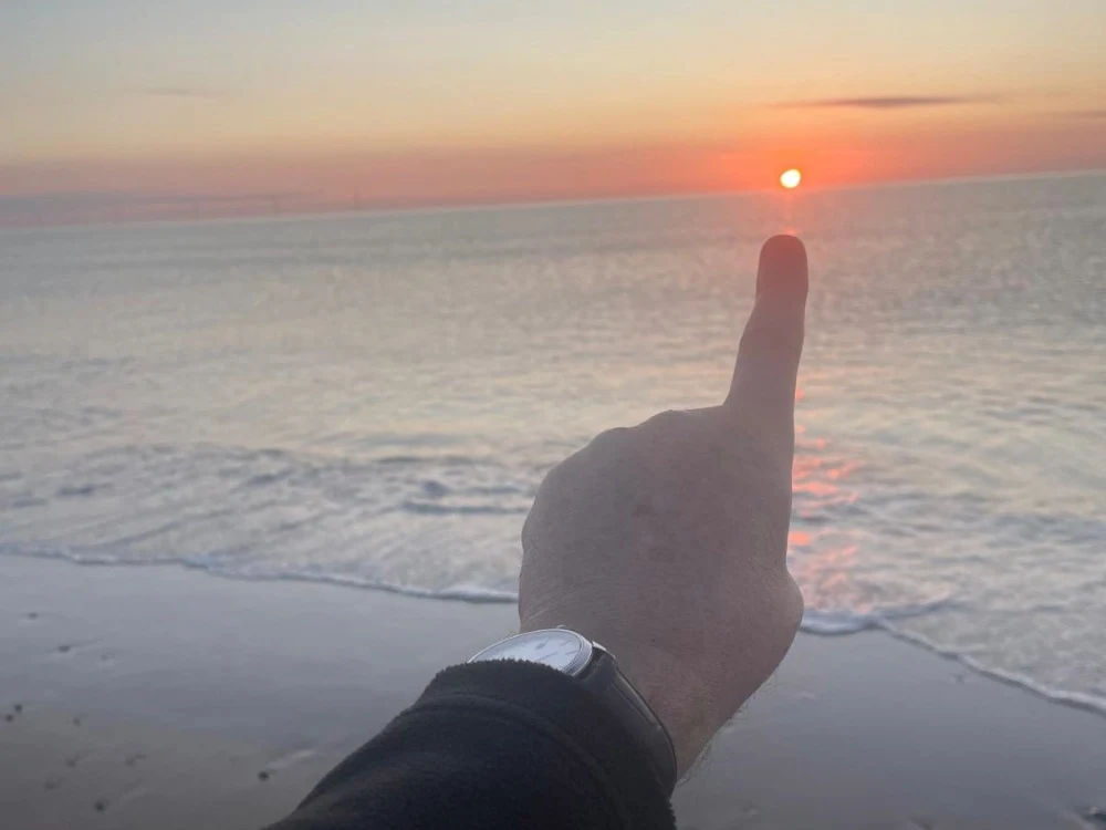 David pointing to the setting sun across the sea.