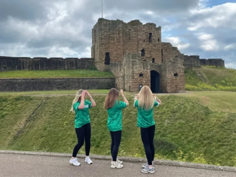 Three women in green t-shirts look at a castle during the Macmillan Half Marathon Hike.