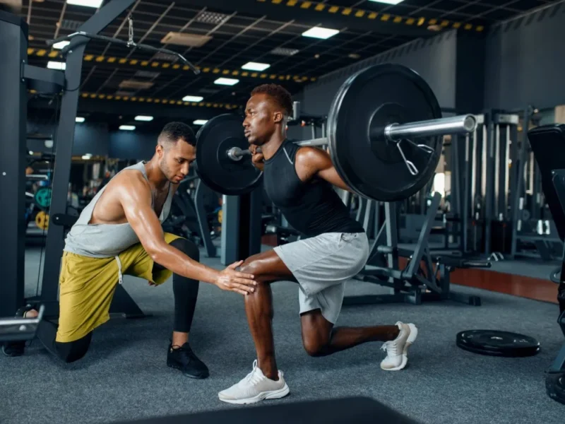 A man spots his friend while he deadlifts in the gym.