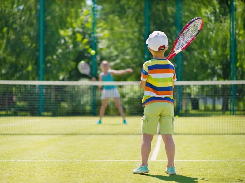 A young boy and a young girl playing tennis on a grass court.
